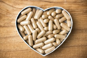 Herbal drug capsules, a heart-shaped box. Wooden surface. Alternative medicine concept.